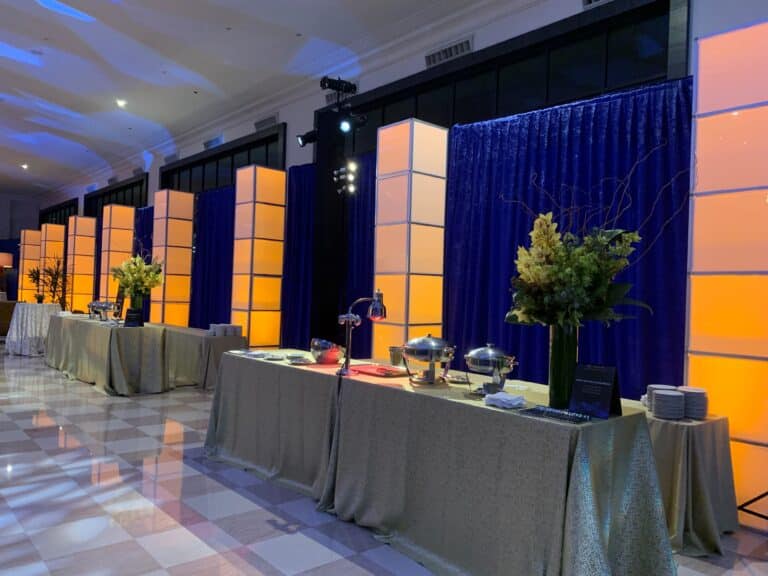 Luxury buffet setup for event with elegant lighting, draped tables, and chafing dishes in a decorated banquet hall.