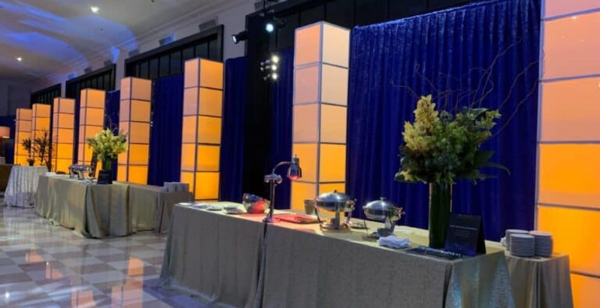 Luxury buffet setup for event with elegant lighting, draped tables, and chafing dishes in a decorated banquet hall.